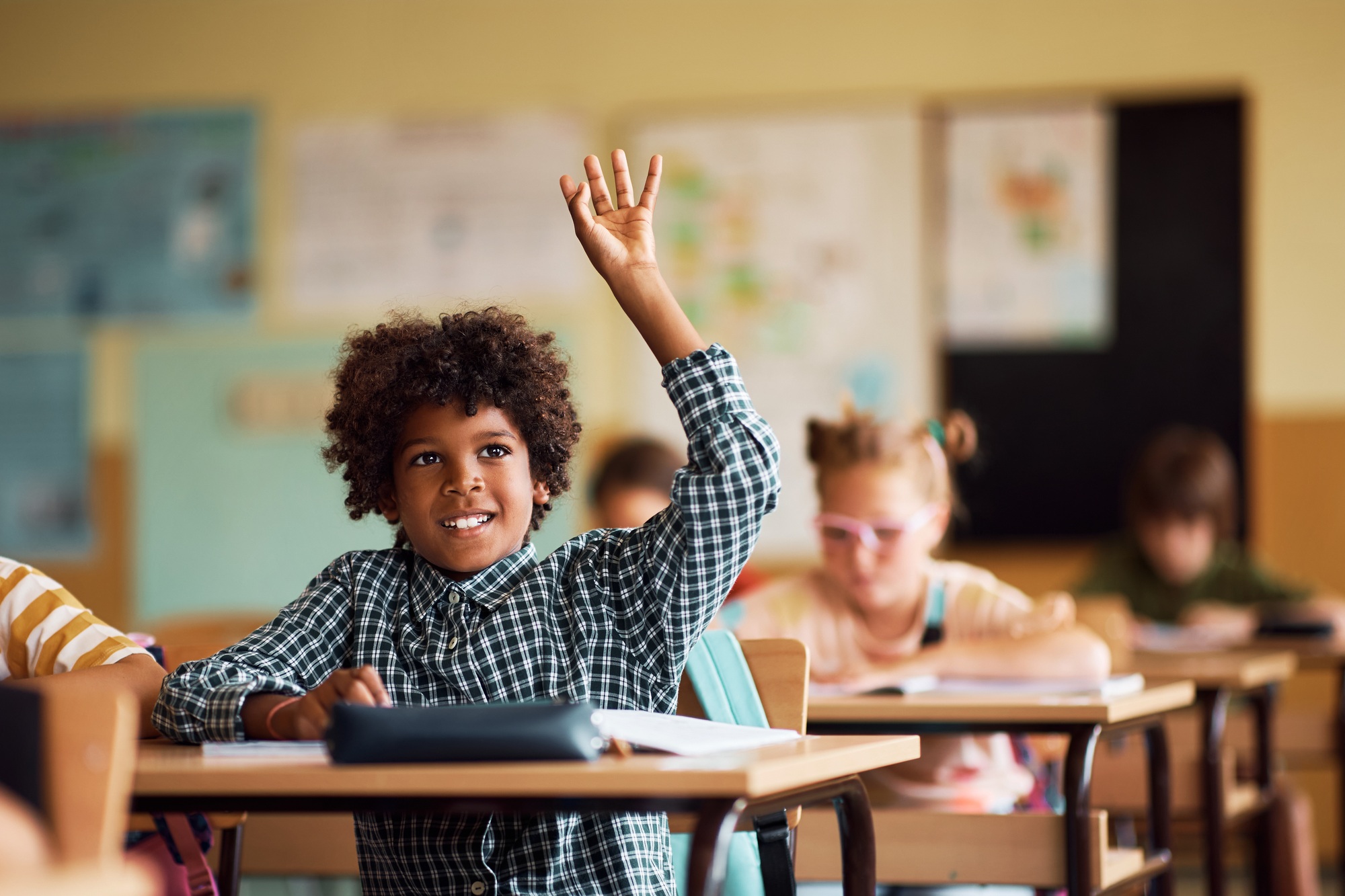 Happy African American kid raising his arm to ask a question during a class at elementary school.